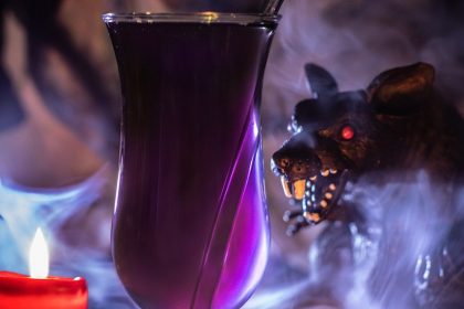 The Witches Cocktail in purple juice surrounded by candles