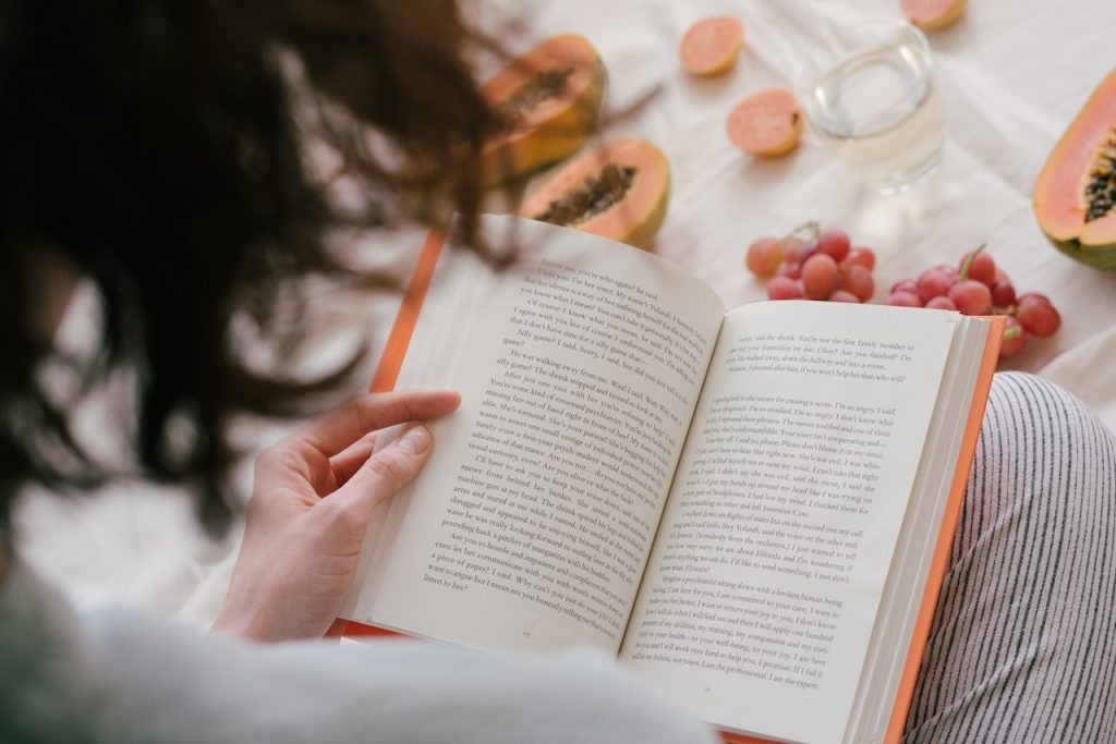 woman reading a book while eating papaya and grapes