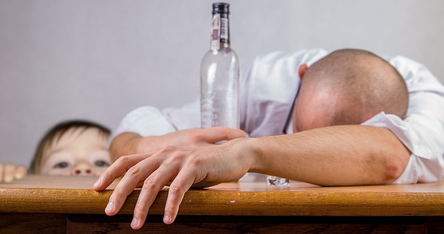 man lies on table drunk being watched by young child