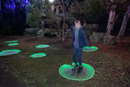 Teenage boy jumps on illuminated lily pads at the Wetland Centre in Barnes posing for mums magazine
